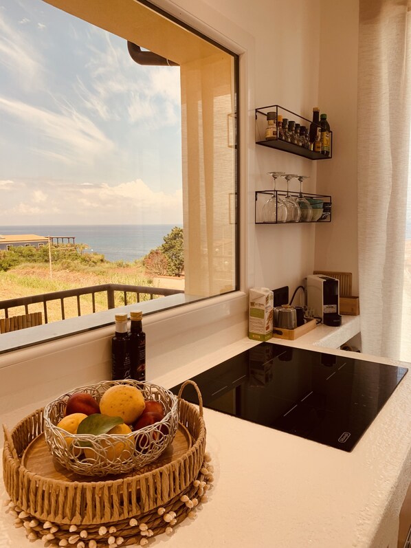 Une cuisine avec vue sur la mer, un panier de fruits et des appareils de cuisine.