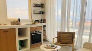 A modern living room with a sofa, a chair, a small table, and a kitchen area with a stove and oven.