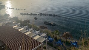 A coastal view with a terrace overlooking the sea, featuring lounge chairs and umbrellas.