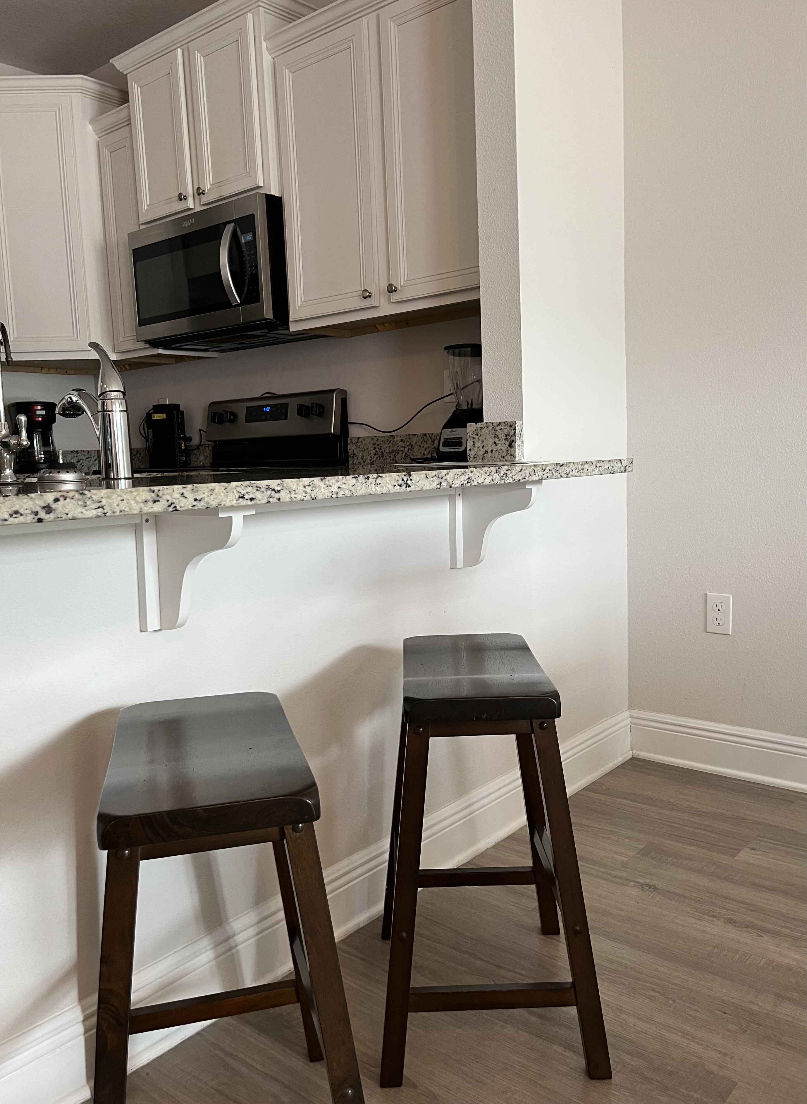 A kitchen with white cabinetry, a microwave, a toaster, and two wooden stools.