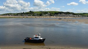 Un bateau appelé BD2 navigue sur une eau calme, près d’une plage, avec des maisons en arrière-plan.