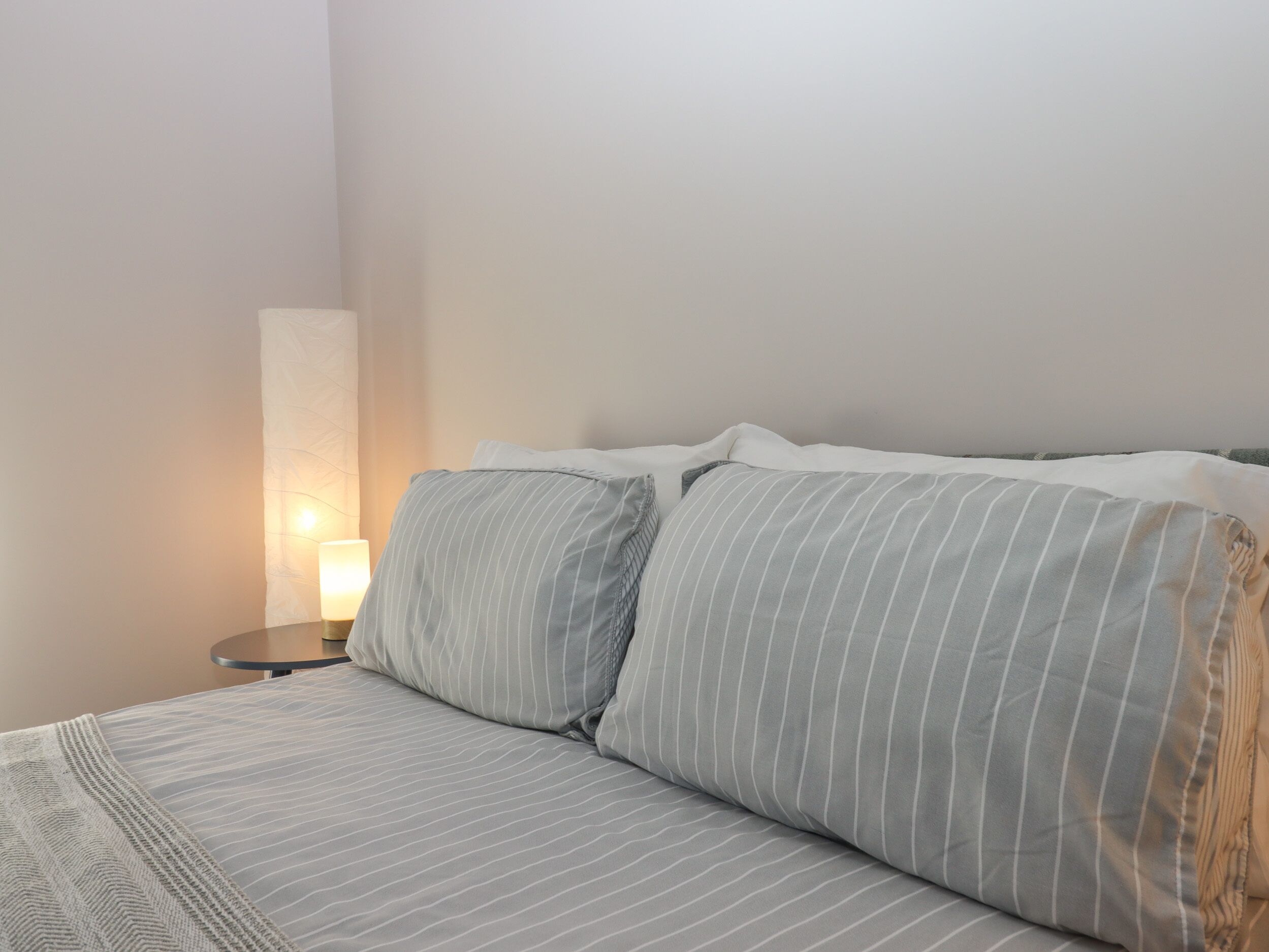 A neatly made bed with striped bedding and a bedside lamp.