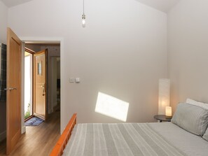 Ein Schlafzimmer mit Bett, Nachttisch, Lampe und einer Tür zu einem anderen Raum.