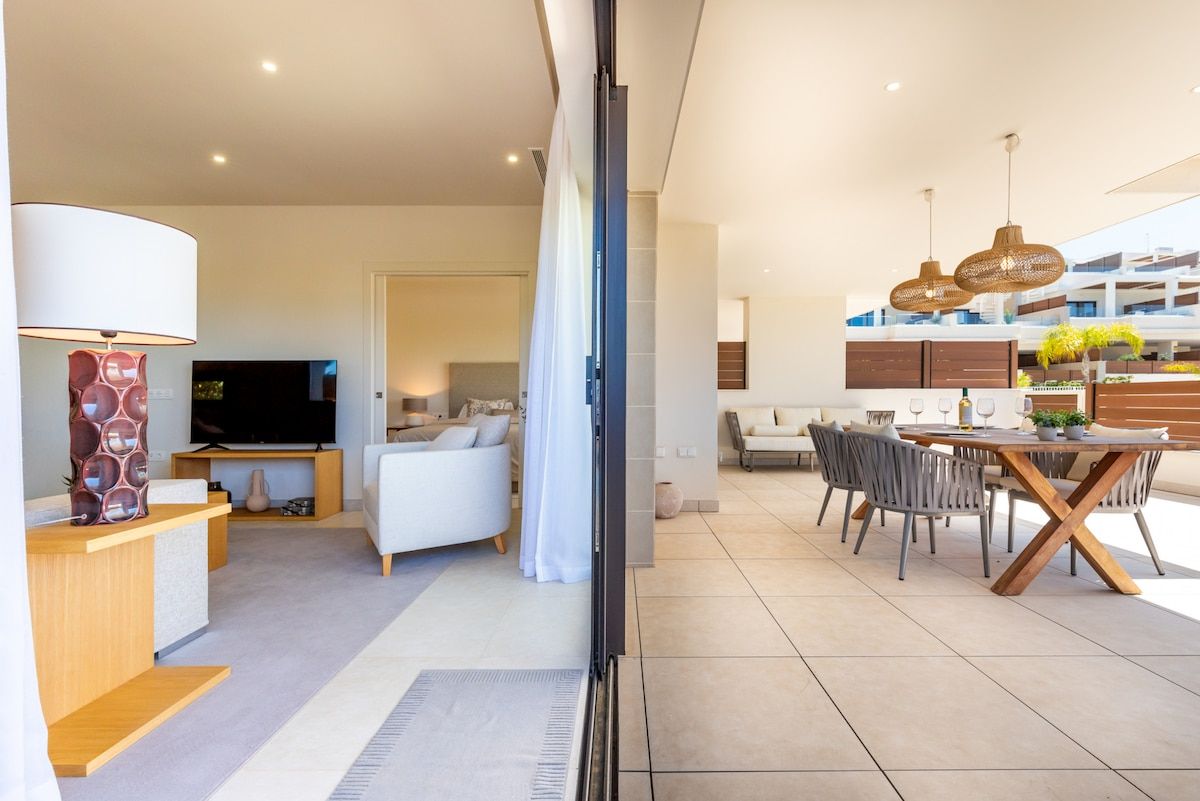 A modern living room with a flat-screen TV, a sofa, and a dining area with a table and chairs.