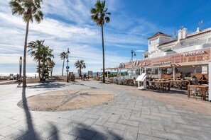 Um calçadão à beira-mar com palmeiras, mesas ao ar livre e um restaurante chamado "Victoria".