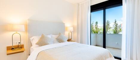 Une chambre d’hôtel avec un grand lit, deux tables de chevet avec des lampes et une vue sur la verdure grâce à une porte-fenêtre coulissante.