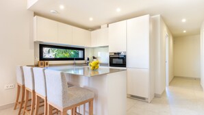 A modern kitchen with white cabinetry, a central island with bar stools, a large flat-screen TV, and a built-in oven. - Jardiana Lotus | Walking distance to La Cala De Mijas (La Cala de Mijas)