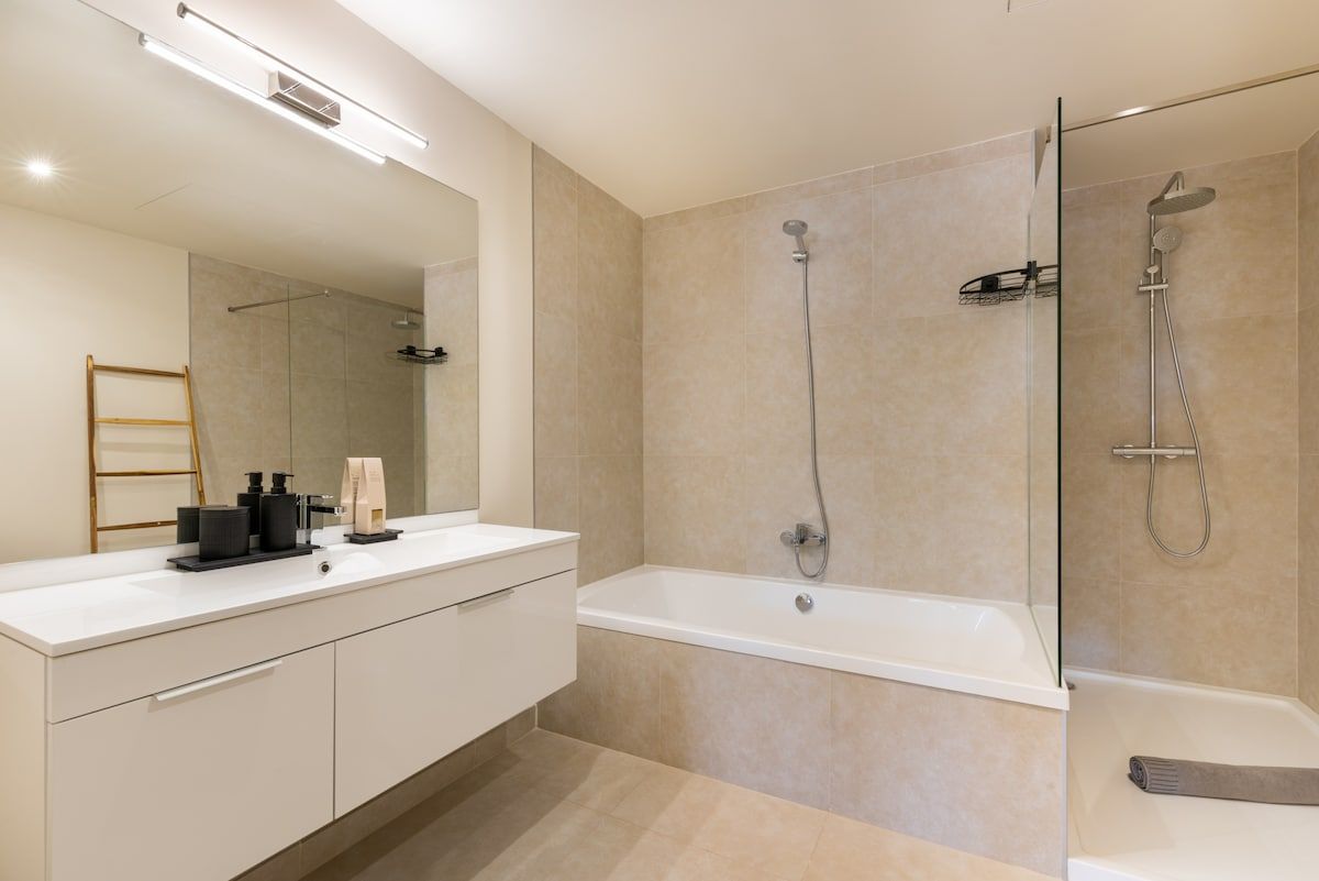 A modern bathroom with a white vanity, a large mirror, a bathtub, and a shower area.