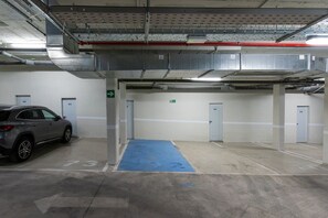 An indoor parking garage with a car parked in a designated space, marked parking spots, and a blue mat leading to an exit.