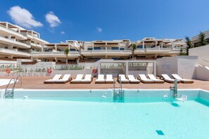 A swimming pool with lounge chairs and a multi-story building in the background.