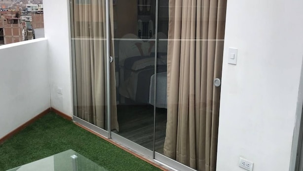 A balcony with a glass table, sliding glass doors, and artificial grass flooring.
