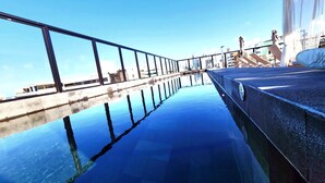 Ein klarer Blick auf ein Schwimmbecken mit Glasboden, umgeben von einem Metallgeländer und einer Betonkante.