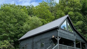 A dark wooden cabin with a sloped roof, a covered porch, and a staircase leading to the entrance. - Private Driftless Cabin w/ Hot Tub, Fireplace & Creekside Views (Ferryville)