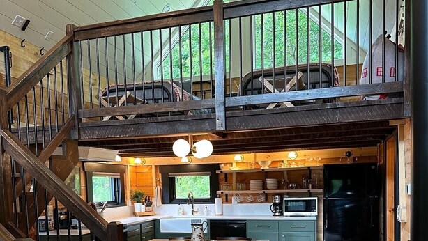 A spacious loft-style kitchen with a dining area, wooden staircase, and a view of the outdoors. - Private Driftless Cabin w/ Hot Tub, Fireplace & Creekside Views (Ferryville)