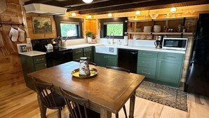 A kitchen with wooden beams, a central island, and a dining table with chairs. - Private Driftless Cabin w/ Hot Tub, Fireplace & Creekside Views (Ferryville)