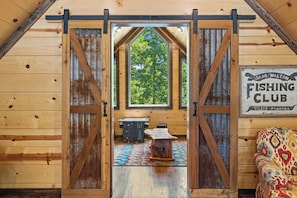 Experience the charm of a rustic cabin with a high ceiling and open doorway leading to a lush outdoor area.