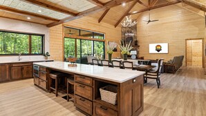 A spacious kitchen with a large island, wooden cabinets, and a stone fireplace. - Bison's Bend in Hochatown/Broken Bow, OK (Broken Bow)