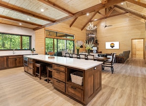 A spacious kitchen with a large island, wooden cabinets, and a stone fireplace.