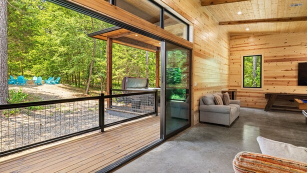 A modern log cabin with a large deck, a cozy living area with a sofa, and a view of a forested area. - Bison's Bend in Hochatown/Broken Bow, OK (Broken Bow)
