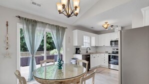 Una cocina moderna con armarios blancos, electrodomésticos de acero inoxidable y una mesa de comedor de vidrio con sillas.