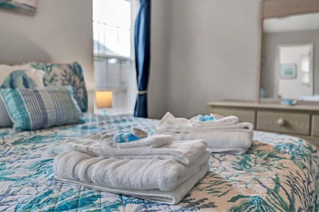 A neatly made bed with a floral bedspread, a folded towel, and a bedside lamp.