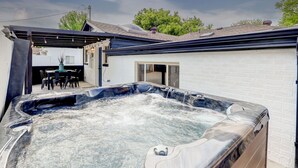 A hot tub in a backyard with a covered patio and a white brick wall. - Hot Tub, Fire Pit, Ping-Pong, 3 min walk to Olde Town Arvada! (Arvada)