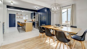 A modern kitchen with dark blue cabinets, a wooden dining table with black chairs, and a large window with curtains. - Hot Tub, Fire Pit, Ping-Pong, 3 min walk to Olde Town Arvada! (Arvada)