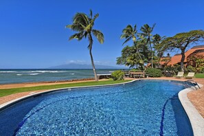 Piscina com vista para o oceano, rodeada por palmeiras e um pátio de tijolos.