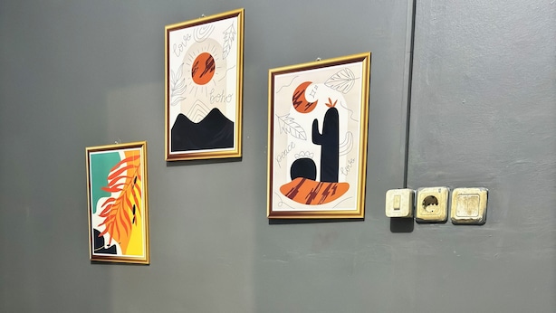 A room with a wooden bench, three framed artworks on the wall, and three electrical outlets. - NgeKost harian (Semarang)