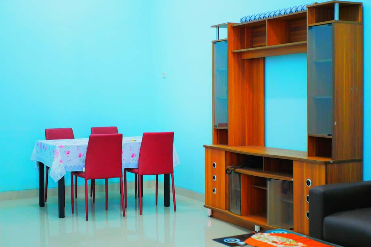 A dining area with a table and chairs, a wooden bookshelf, and a black sofa.