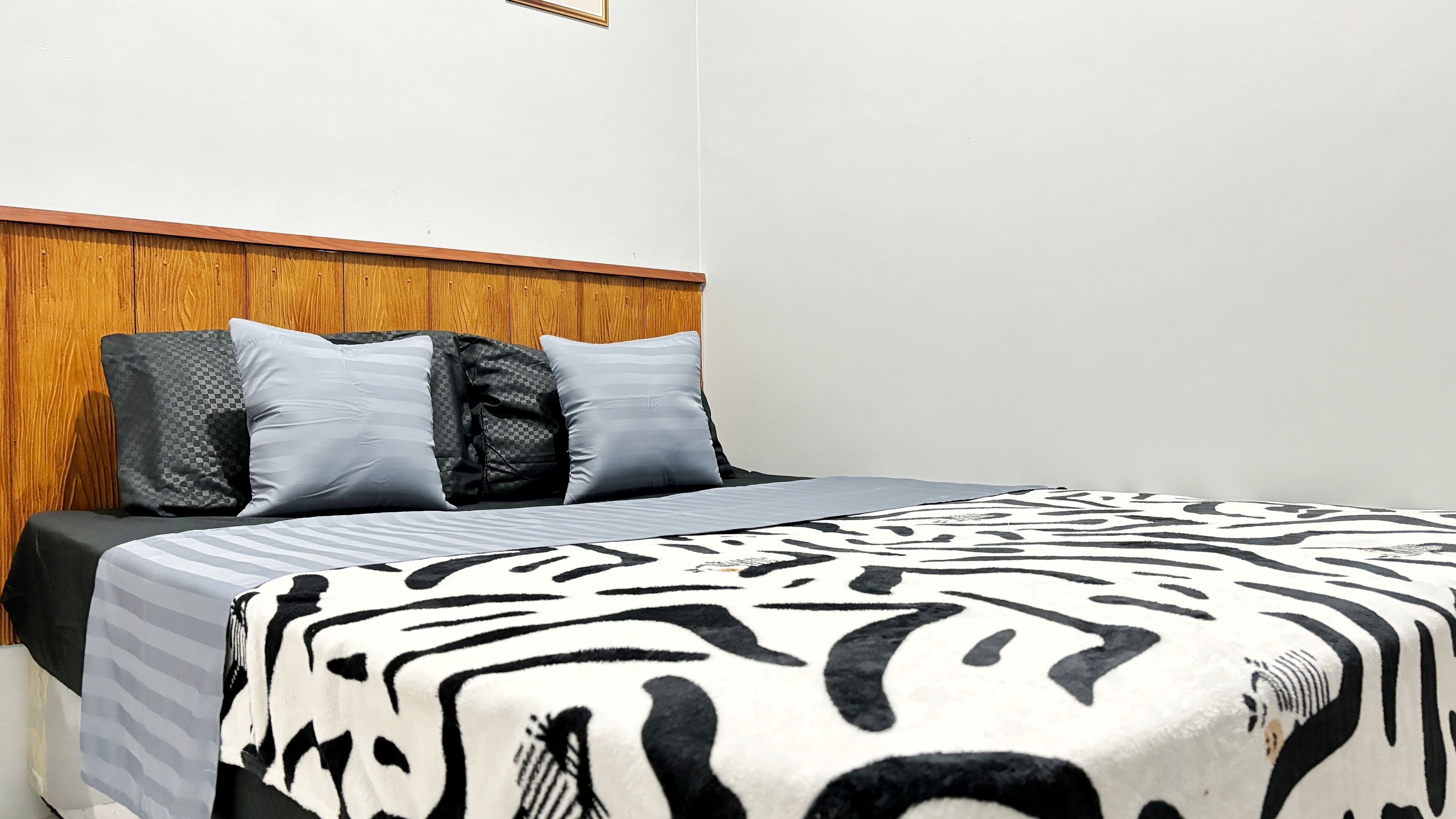 Ett hotellrum med en sänggavel i trä, en säng med ett zebra-mönstrat överkast och två kuddar med ett rutmönster.