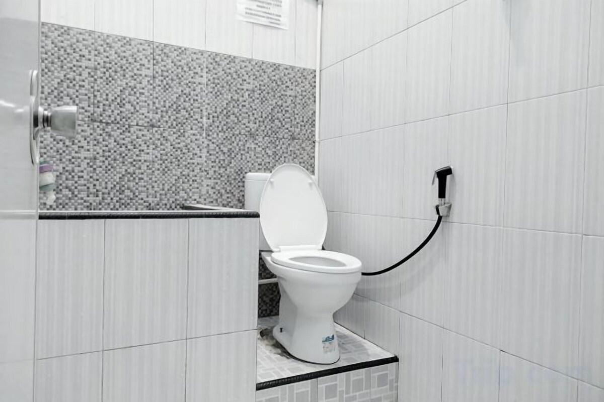 A toilet with a bidet attachment, a tiled wall, and a door.