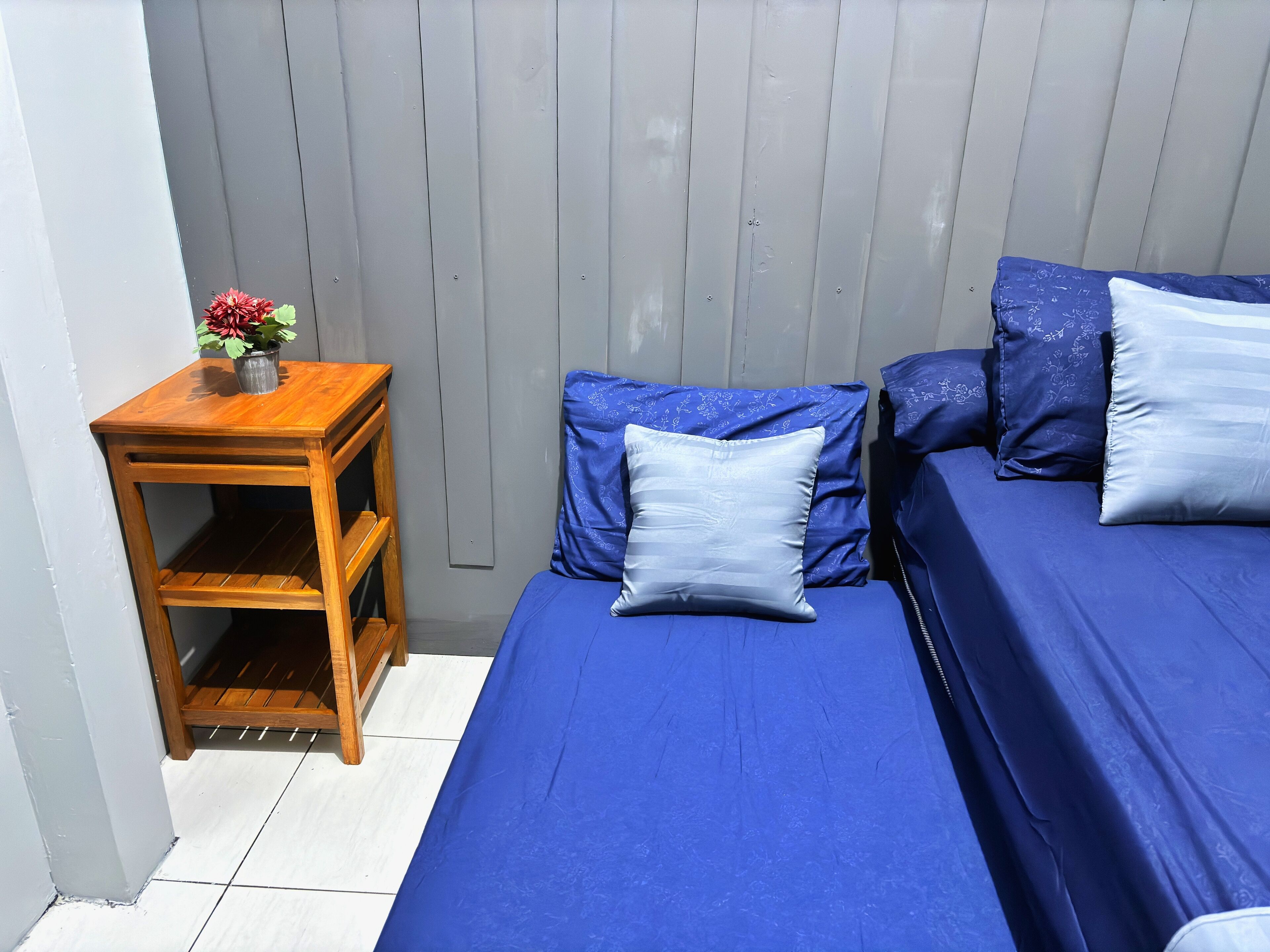 Een kleine, afgesloten kamer met een bed, een nachtkastje en een bloempot.
