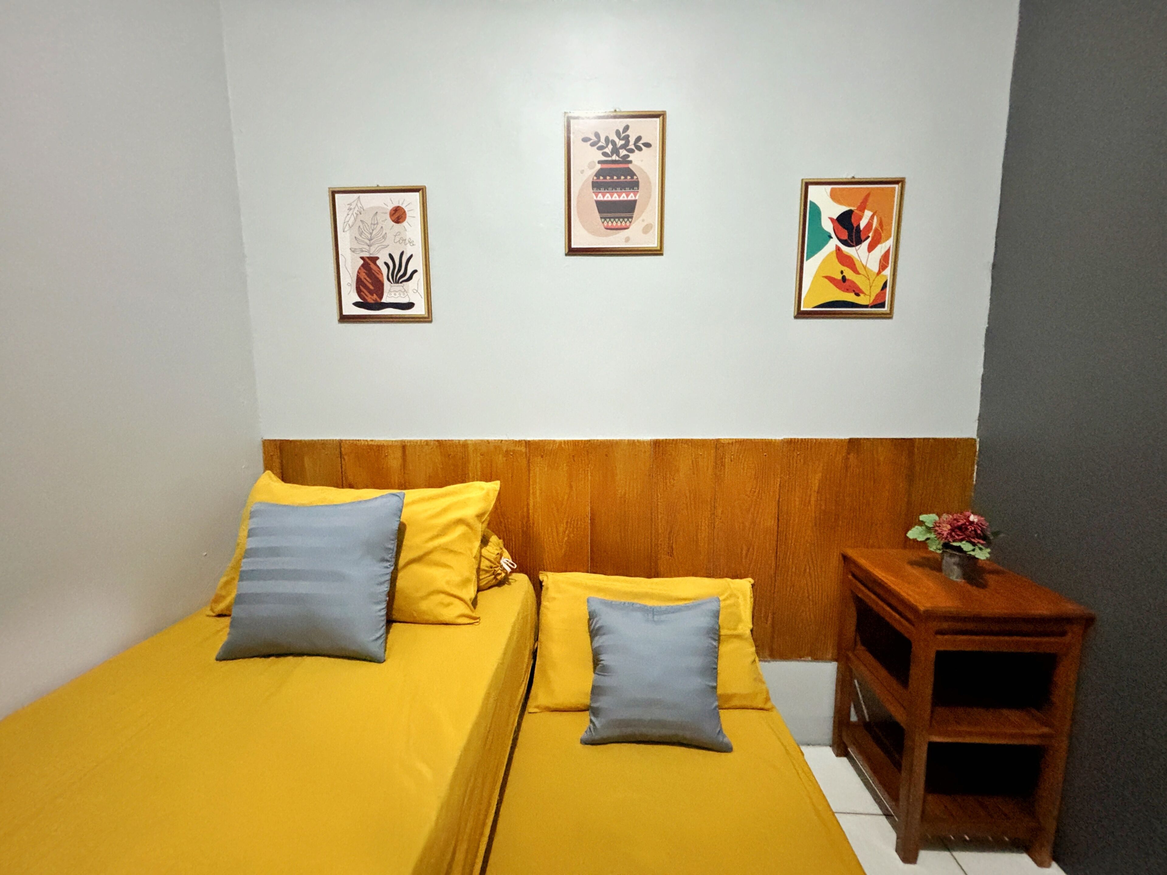 A room with two beds, wooden headboard, and three framed artworks on the wall.