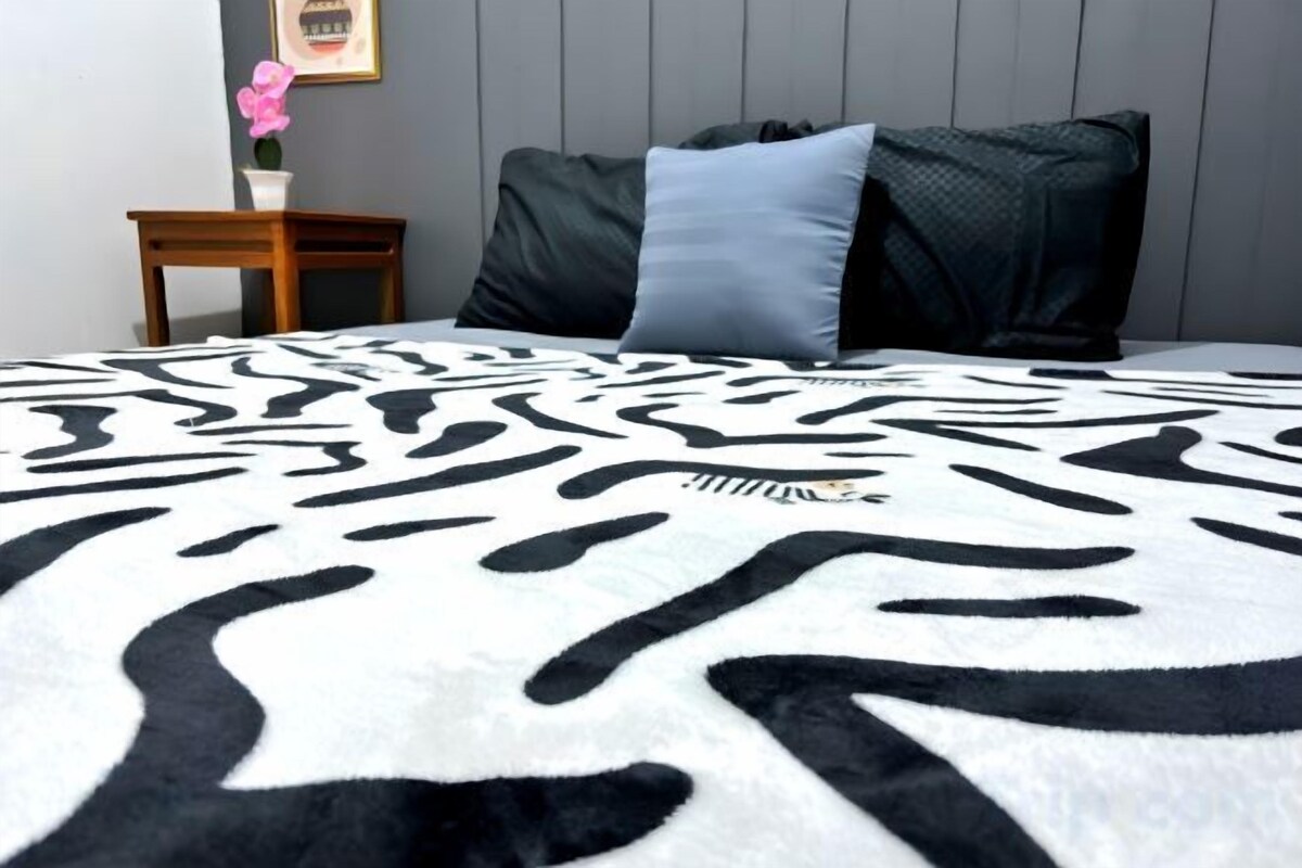 A bed with a zebra print blanket, a dark pillow, and a small wooden nightstand with a vase of flowers.