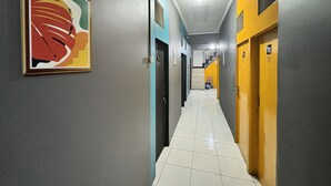A hallway with a tiled floor, doors, and a framed artwork on the wall. - NgeKost harian (Semarang)