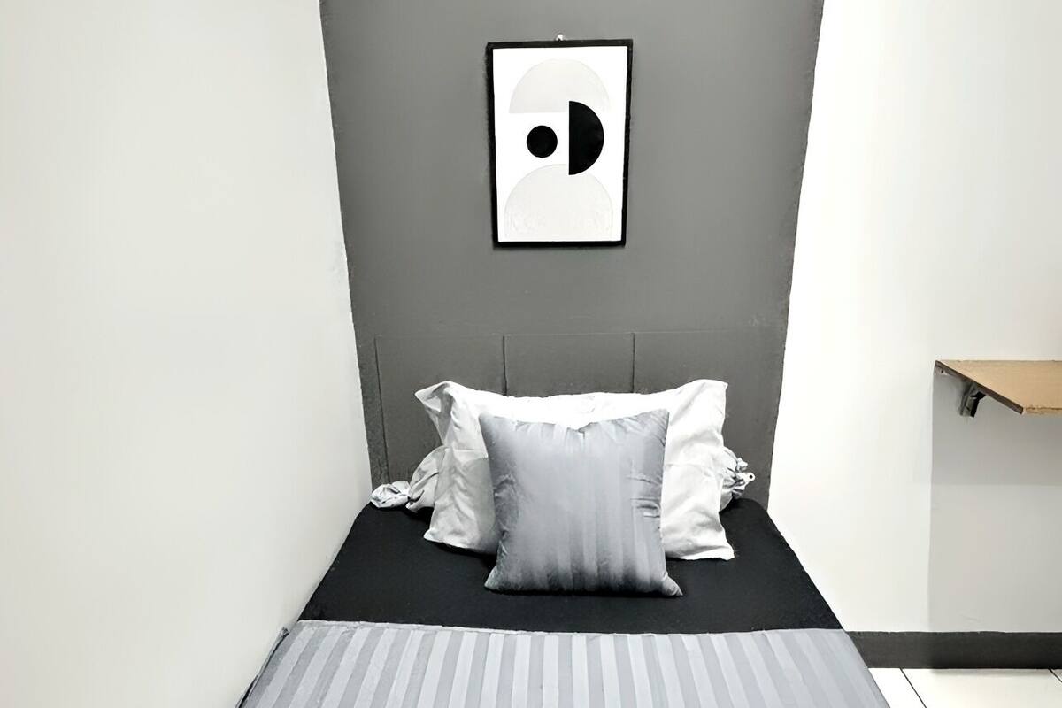 A small, modern bedroom with a bed, pillows, and a wall-mounted picture.