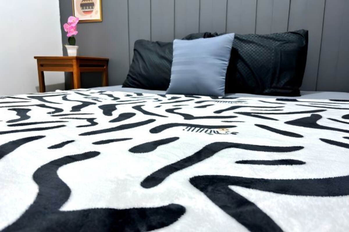 A bed with a zebra print blanket, a small wooden nightstand with a vase of flowers, and a framed picture on the wall.