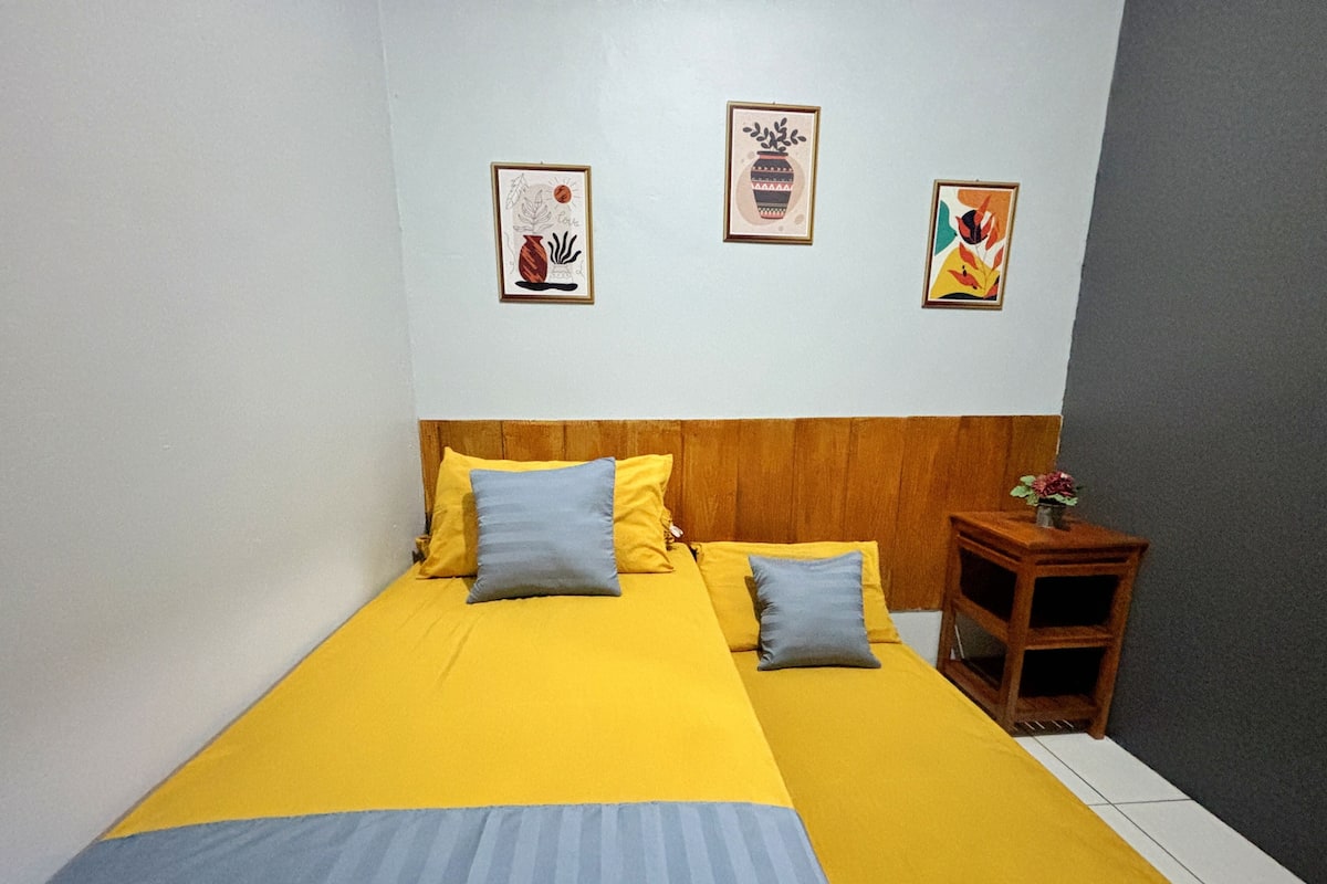 A bed with yellow and blue bedding, a wooden headboard, and a nightstand with a vase.