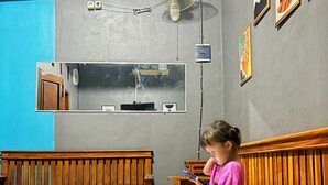 A room with a wooden bench, a wall-mounted fan, and framed artwork. - NgeKost harian (Semarang)