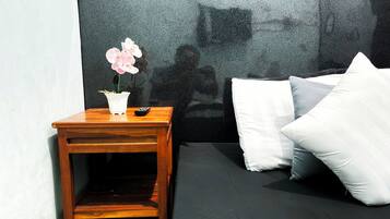 Une chambre à coucher avec un lit, des oreillers, une table de chevet, une télécommande et une orchidée en pot.