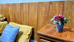 A wooden table with a potted plant, a blue pillow, and a yellow cushion against a wooden wall. - NgeKost harian (Semarang)