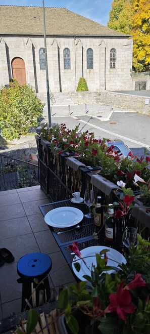 An outdoor dining area with tables set for two, a stone building in the background, and a metal fence with flowers. - Gîte le Fortunio-Gîte-Family-Ensuite with Bath (RIEUTORT DE RANDON)