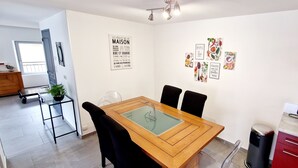 A modern kitchen with a wooden table, black chairs, and a red cabinet. There is a black kettle on the counter and a potted plant on a black metal stand.