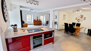 Une cuisine moderne avec des meubles de rangement rouges, un four encastré et un coin repas comprenant une table et des chaises en bois.