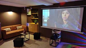 A modern living room with a sofa, coffee table, and a projector screen displaying a scene.