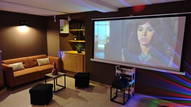 A modern living room with a sofa, coffee table, and a projector screen displaying a scene. - Gîte le Fortunio-Gîte-Family-Ensuite with Bath (RIEUTORT DE RANDON)