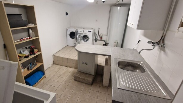 A small laundry room with a washing machine, a sink, and shelves with cleaning supplies.