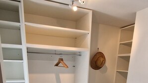 A walk-in closet with open shelves, a hat on the wall, and a wooden hanger.