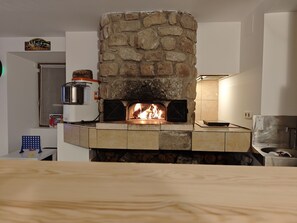 Ein Kamin aus Stein mit Holzofen, einem Wasserkocher und einem Halter dafür an der Wand.